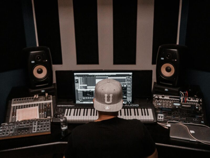 Musikproduzent am Schreibtisch eines Homestudios mit Studiomonitoren, Keyboard und Mischpult.