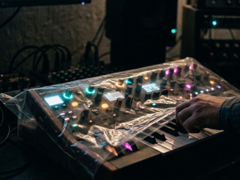 Ein Korg-Synthesizer unter transparenter Folie mit beleuchteten Reglern in einem dunklen Studio.