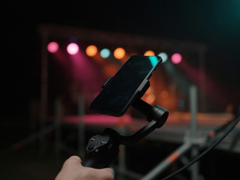 Smartphone auf einem Gimbal an einem Videoset, dahinter bunte Bühnenscheinwerfer (KI-generiert)