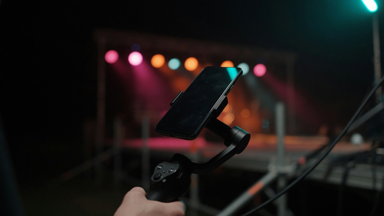 Smartphone auf einem Gimbal an einem Videoset, dahinter bunte Bühnenscheinwerfer (KI-generiert)